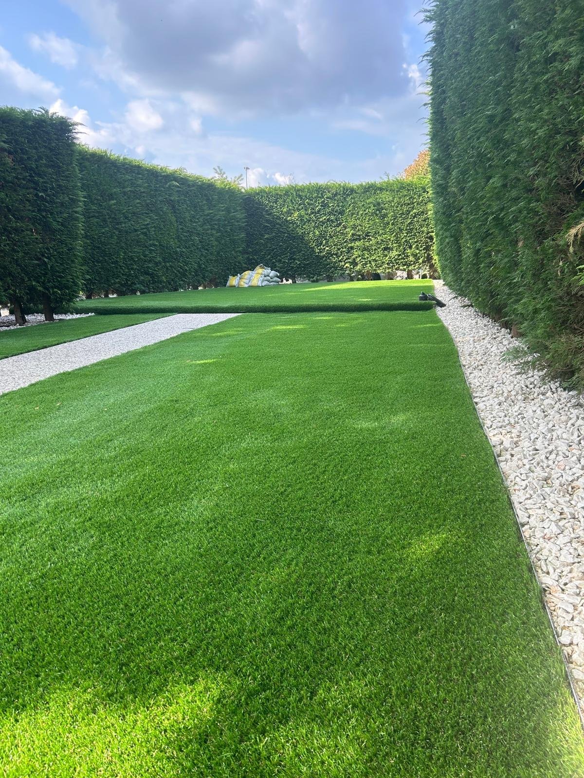 Giardino curato con prato verde, siepi alte e vialetti in ghiaia bianca