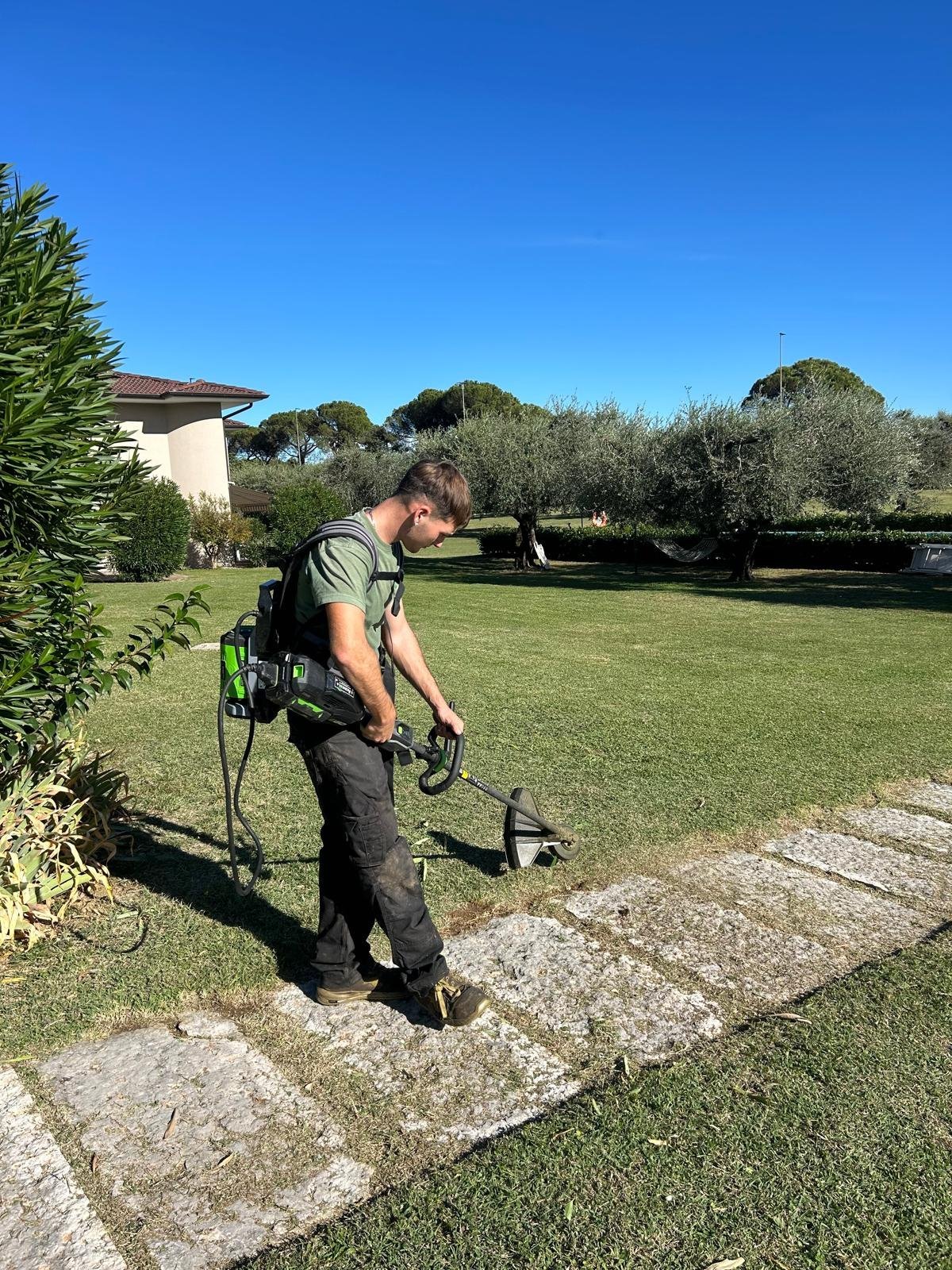 Operatore con decespugliatore a batteria che rifinisce il bordo del prato vicino a un vialetto in pietra