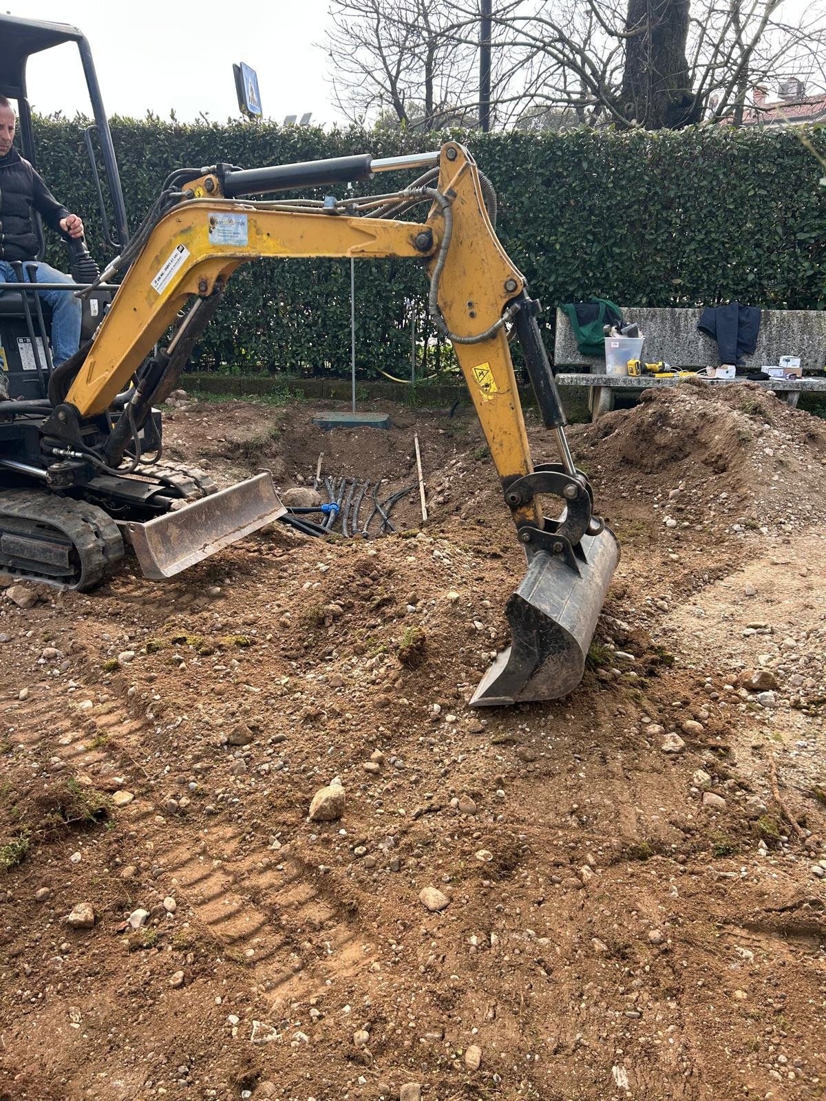 Mini escavatore giallo al lavoro in un cortile sterrato in contesto residenziale